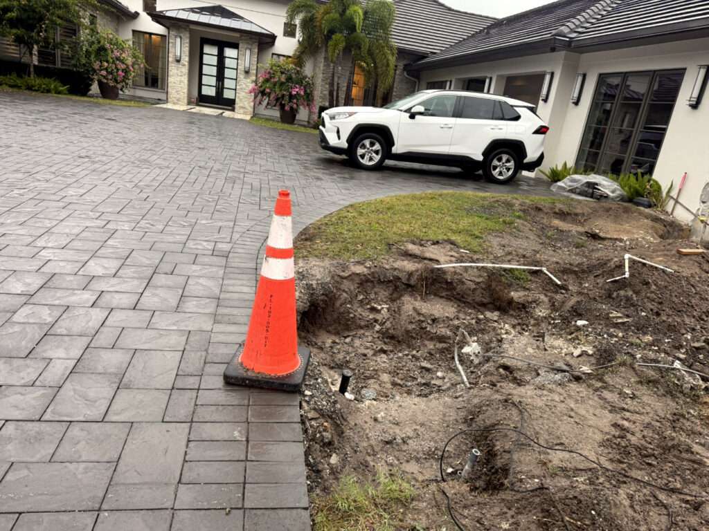 residential construction site with open ground excavation and safety cone near driveway