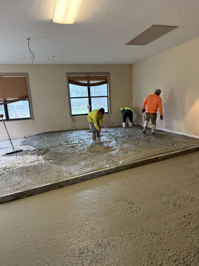 construction crew pouring and leveling fresh concrete floor inside building