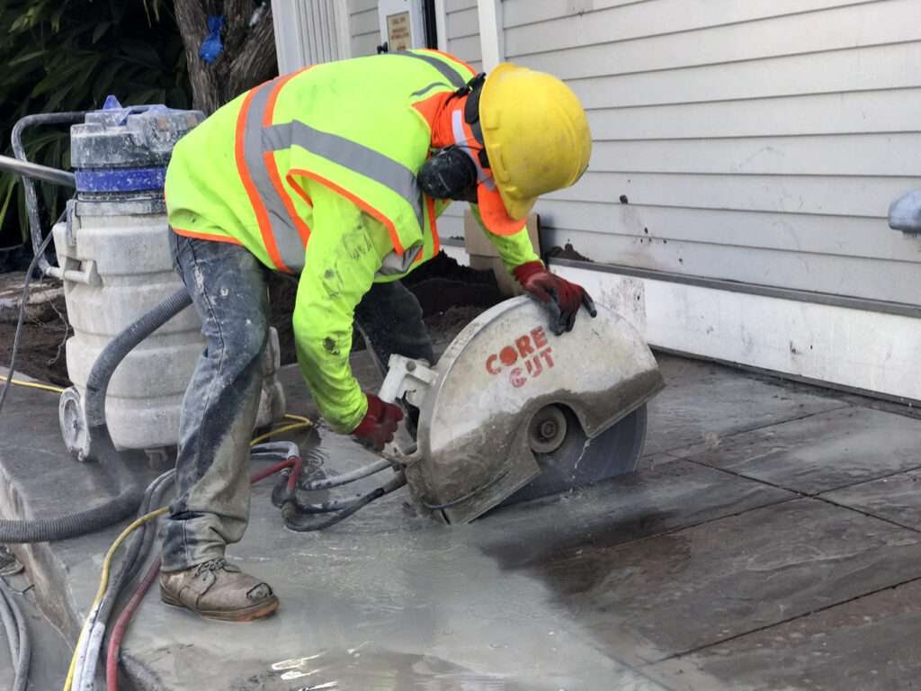 worker using hand saw for concrete cutting on residential driveway with safety equipment