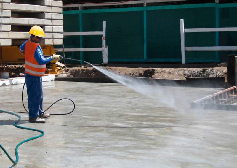 Construction worker spraying water to cure a fresh concrete slab on a job site